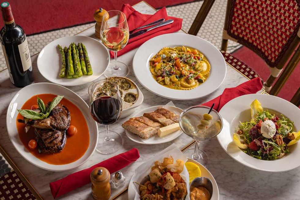 A bottle of wine and white plates of asparagus, escargots, ravioli and lamb