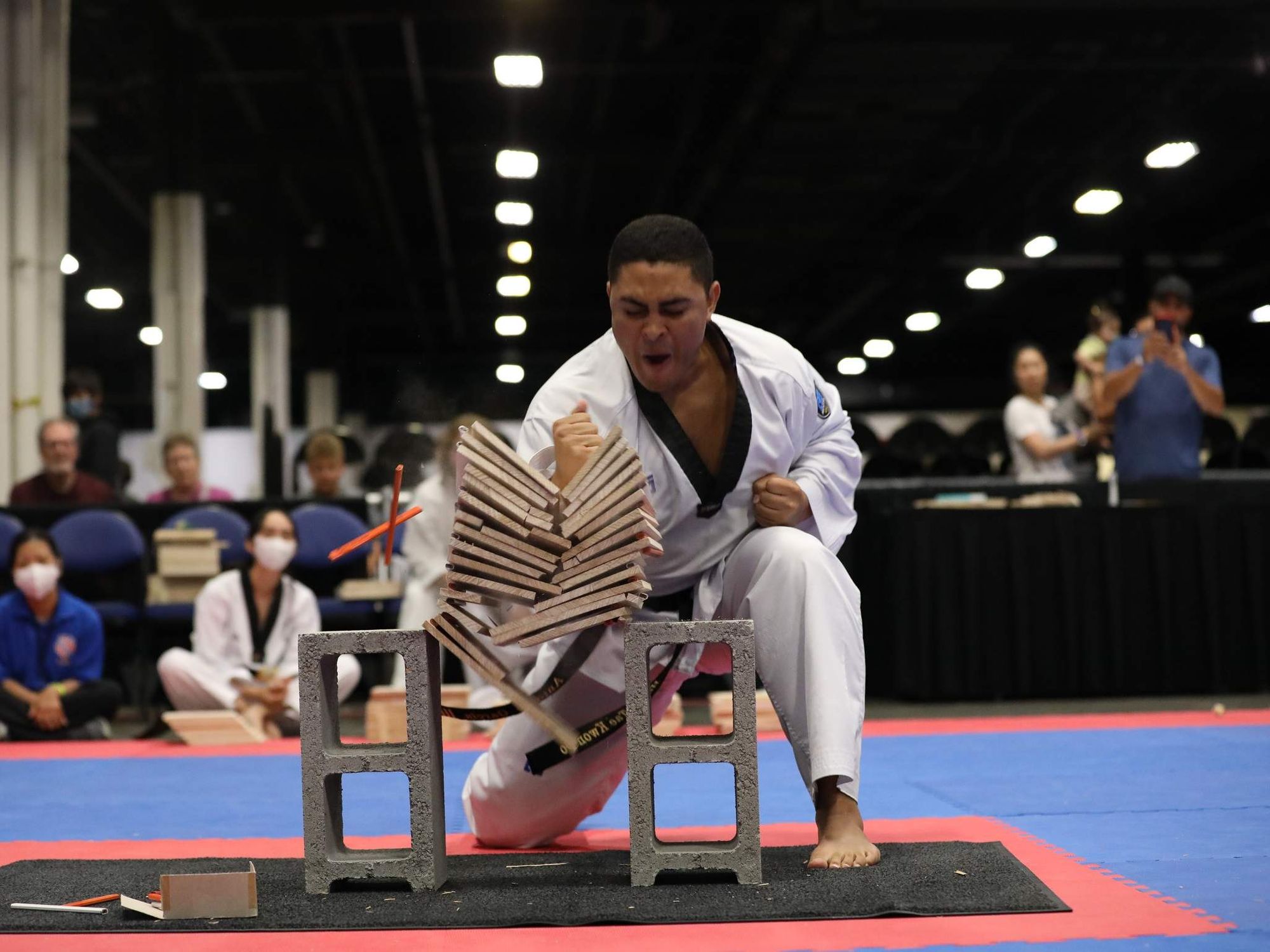 A boy in a gi breaks a stack of boards in a sports arena