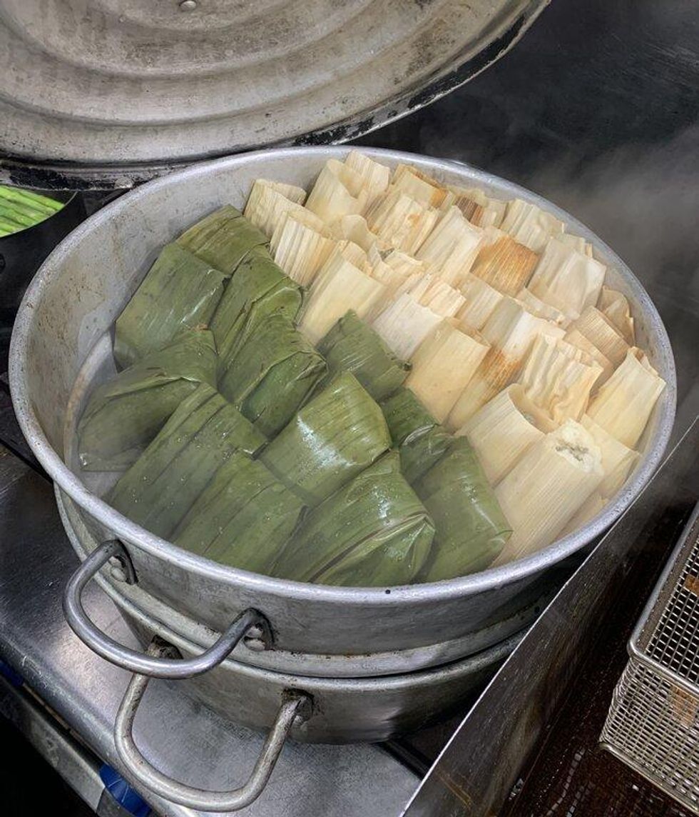 A double metal pot of tamales with green and corn-colored husks