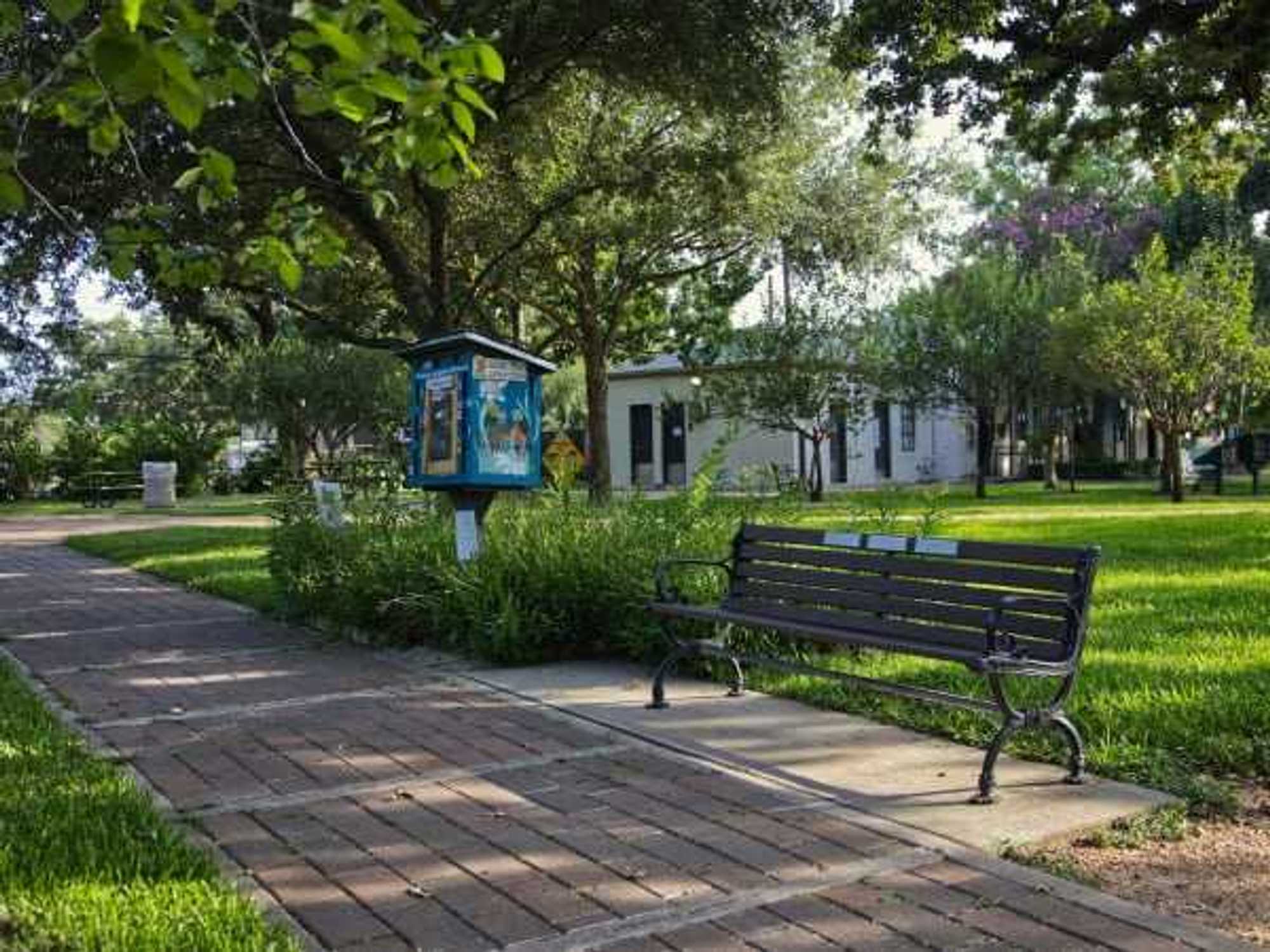 A Houston park with a bench and a little free library