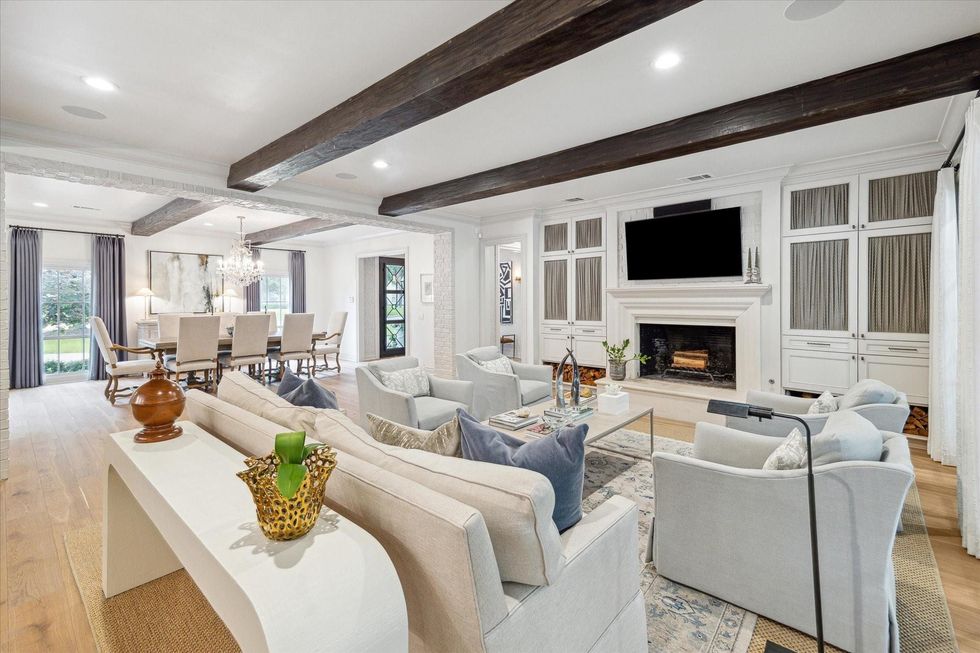 A living room with a sofa facing the fireplace, with two chairs on either side of it, and a dining room in the background at left.