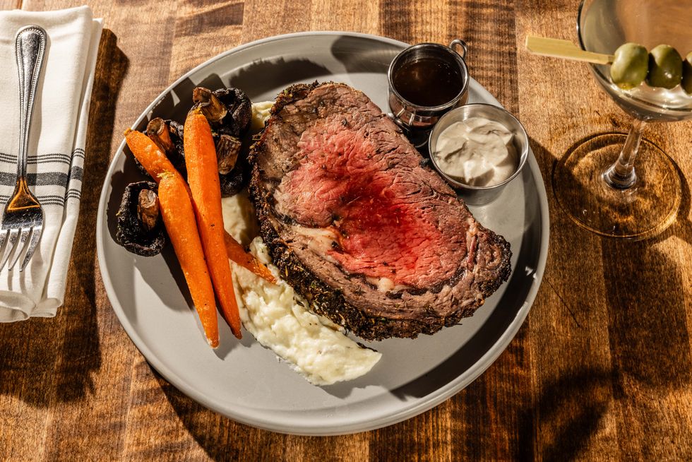 A round gray plate with a slab of medium rare prime rib potatoes and carrots