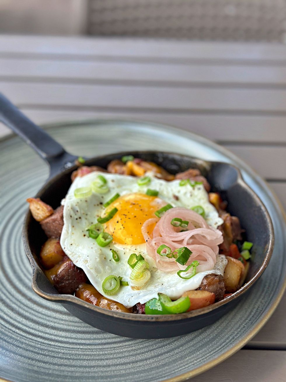 A skillet filled with potatoes, an over-easy egg, green onions, and a barbecue brisket.