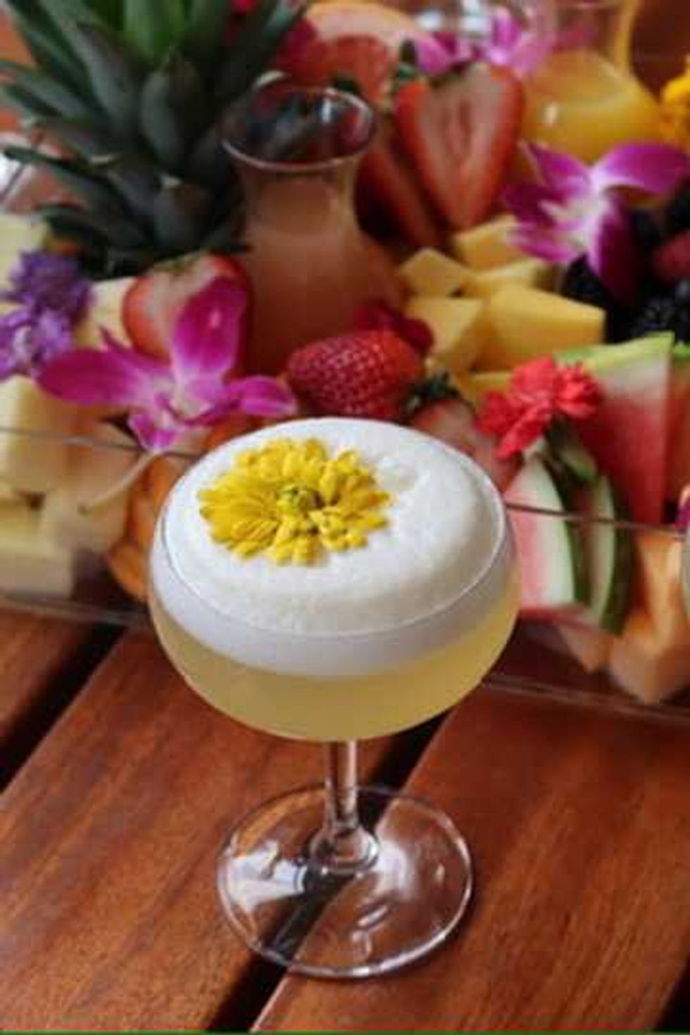 A sparkling cocktail on a table with fruit in the background.