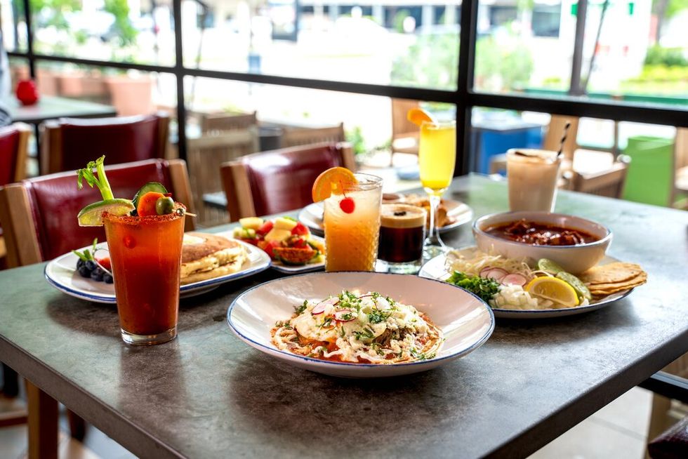 A table of brunch dishes, including heuvos ranchers, a Bloody Mary and mimosas.