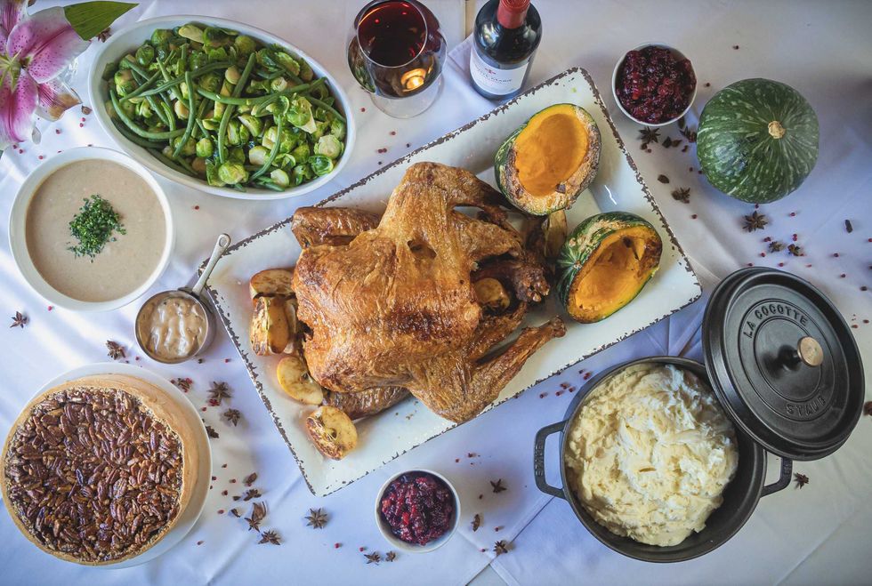 A turkey on a platter surrounded by a pecan pie, mashed potatoes, greens, and cranberry sauce.
