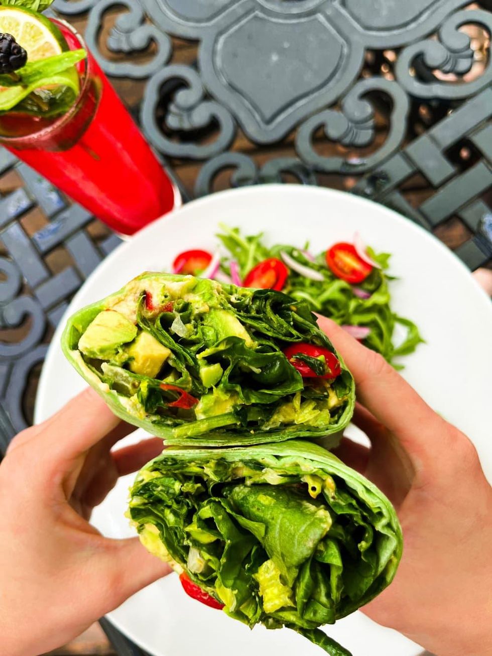 A wrap filled with lots of greens, and a side salad with tomatoes.