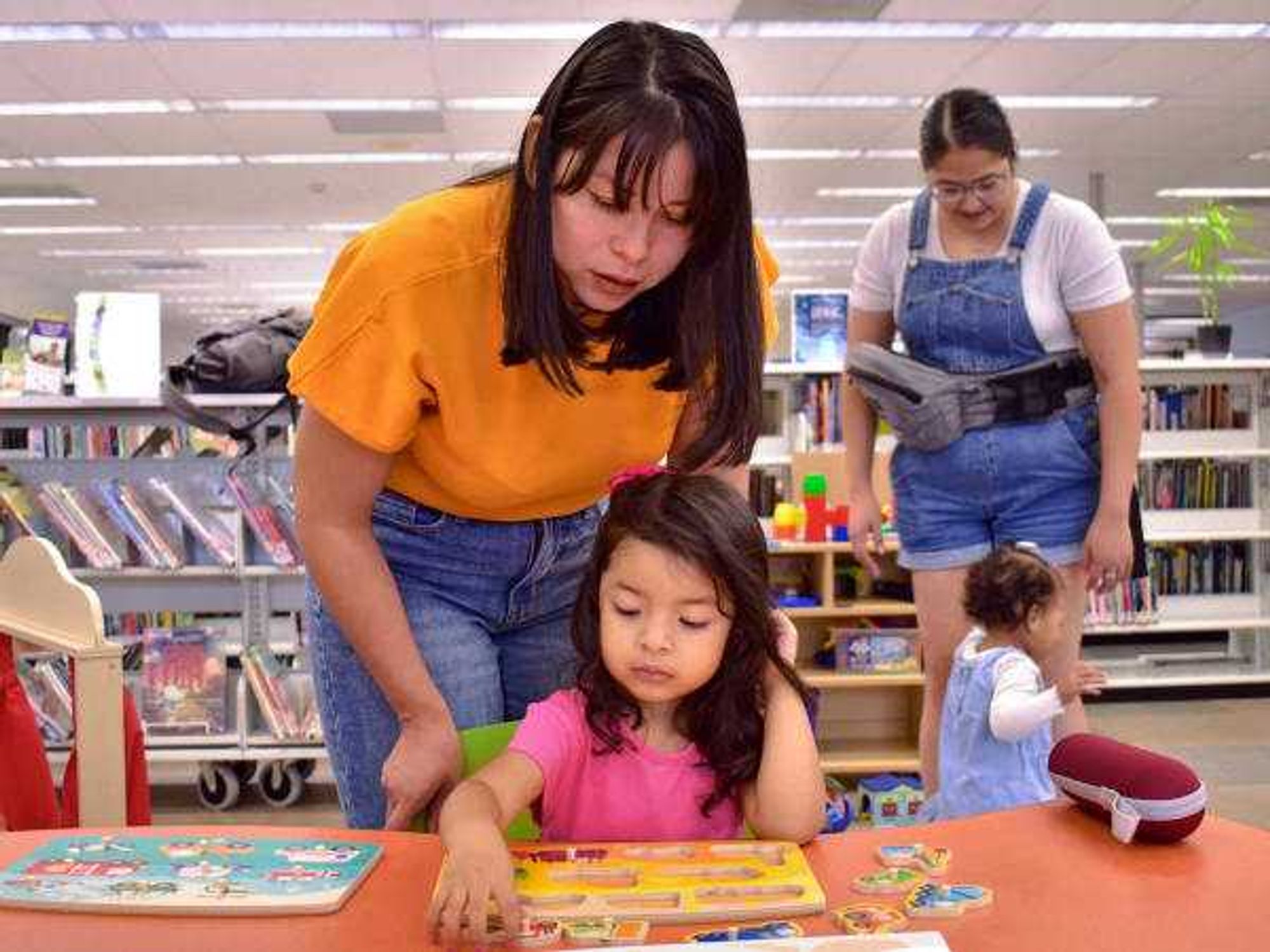 A young girl reads in a Family Place Library win Houston while caretakers look on.