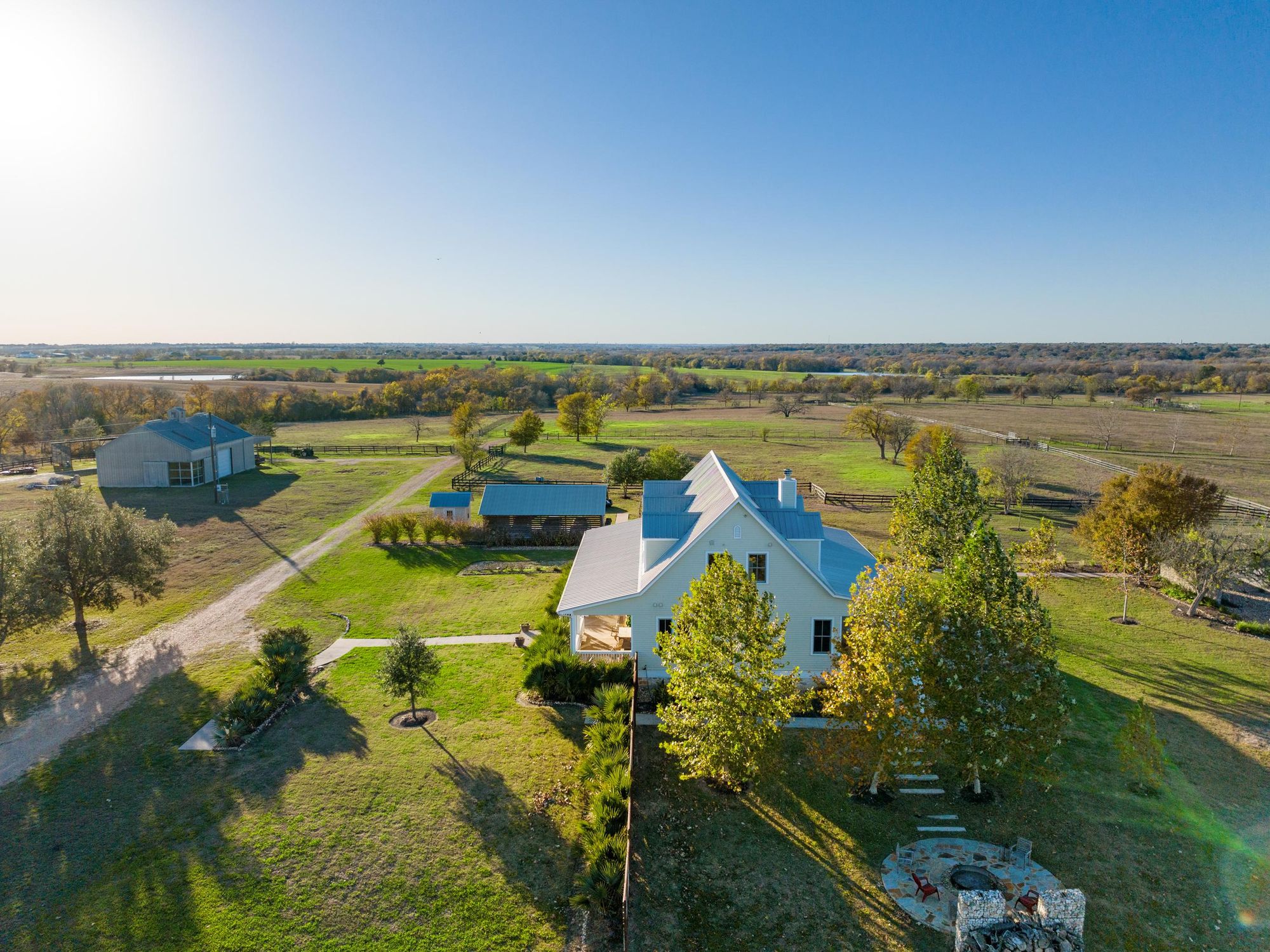 Ariel image of Big Step Ranch, with a farmhouse and outdoor fire pit in the foreground, and outdoor kitchen, outbuilding and rolling hills in the background.
