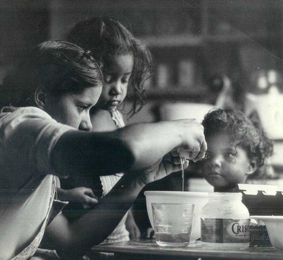 Black and white photo by Nat Brown showing a woman and children baking in a kitchen