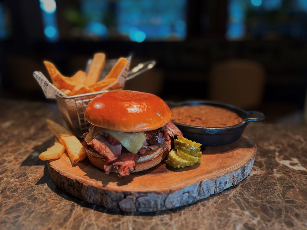 Brisket sandwich with fries and a crock of baked beans on a wooden slab.