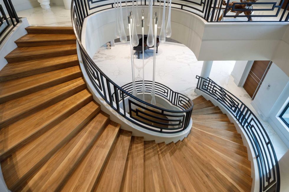Detail of the sweeping spiral staircase of 3201 Noble Lakes Lane, showing its blonde wood steps and iron wood railing
