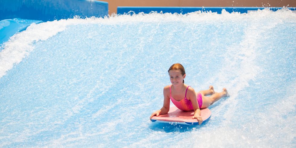 Girls riding a boogie board down a water wave.