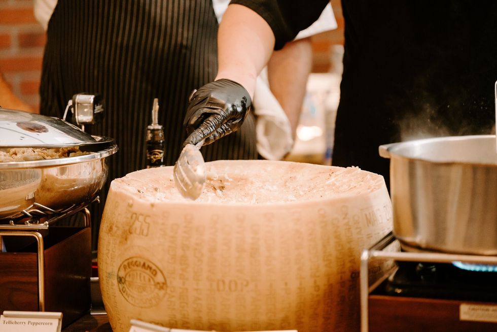 Image of a hand scooping pasta out of a giant wheel of Parmesan cheese