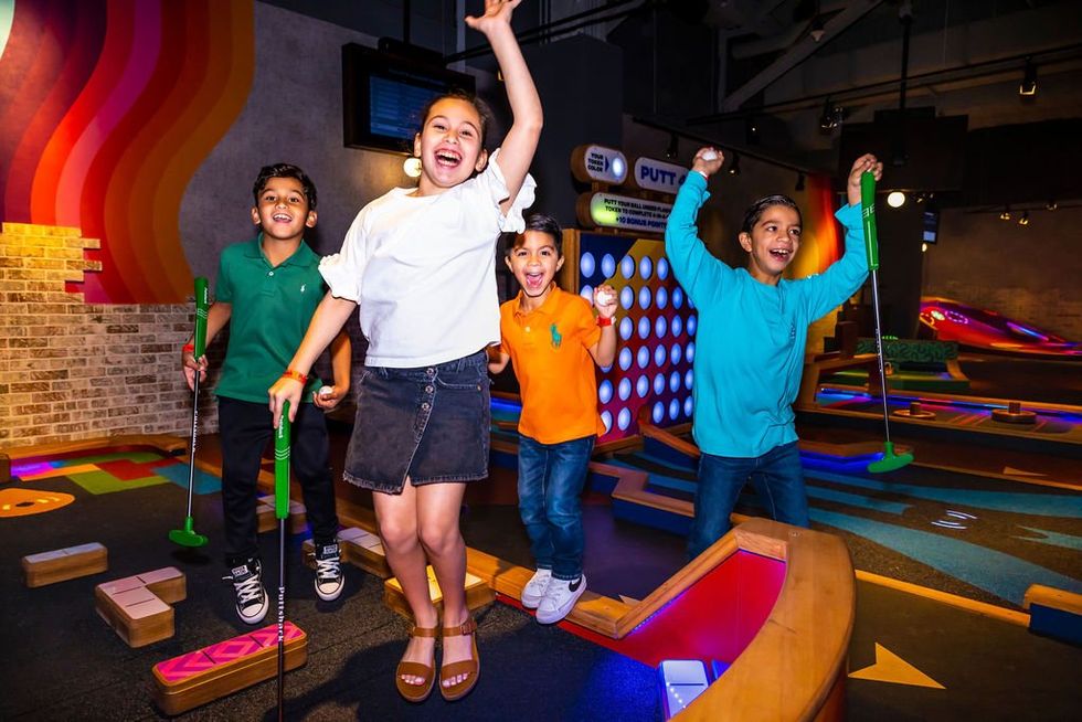Kids with putters, jumping up and looking happy at an indoor miniature golf course