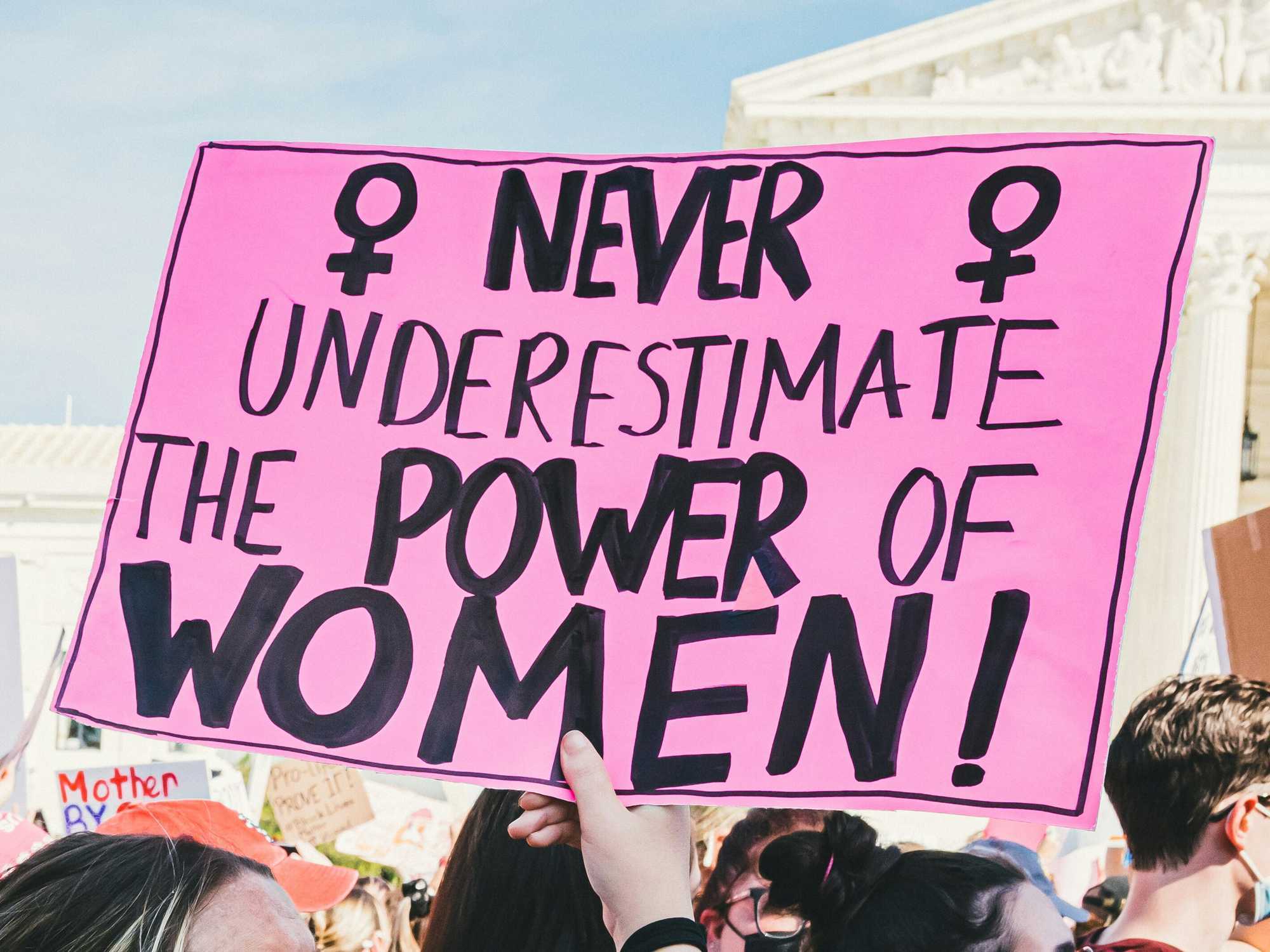 Person holding a sign at a protest that states, "Never underestimate the power of women!"