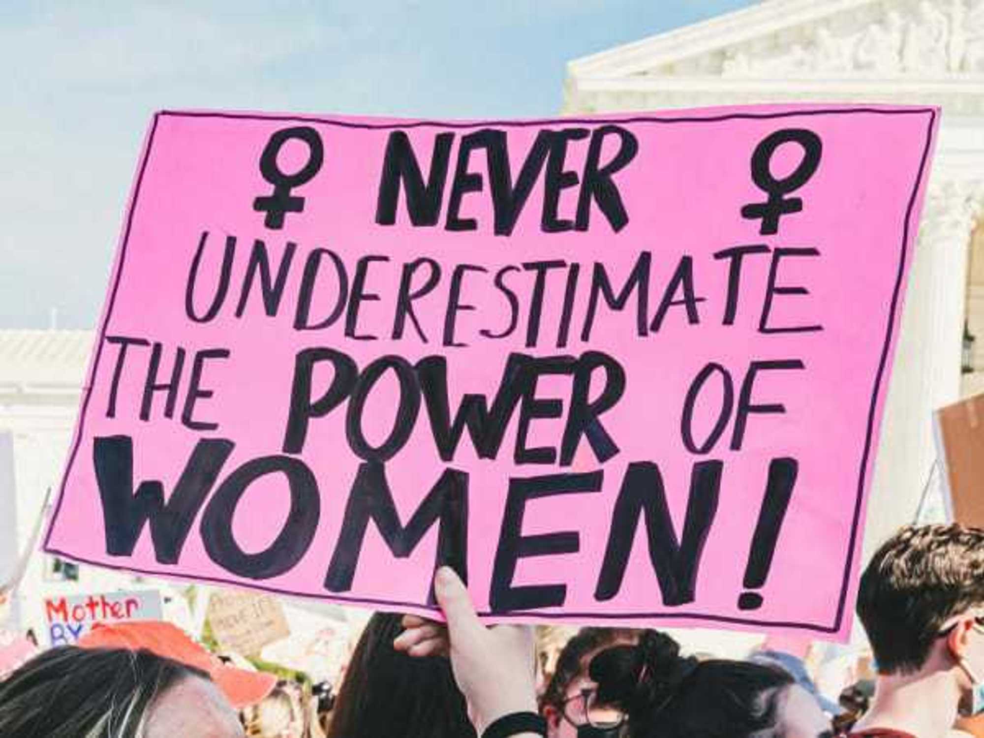 Person holding a sign at a protest that states, "Never underestimate the power of women!"