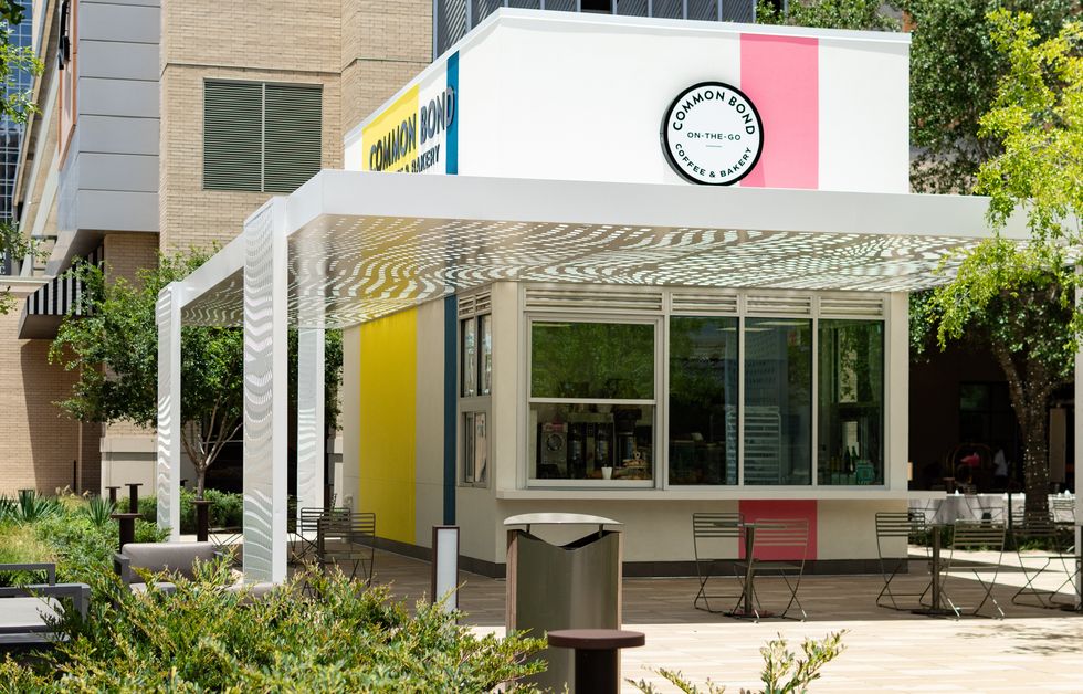 Photo of a square-shaped building with Common Bond written on it, sitting amid trees, a plaza and outdoor folding chairs