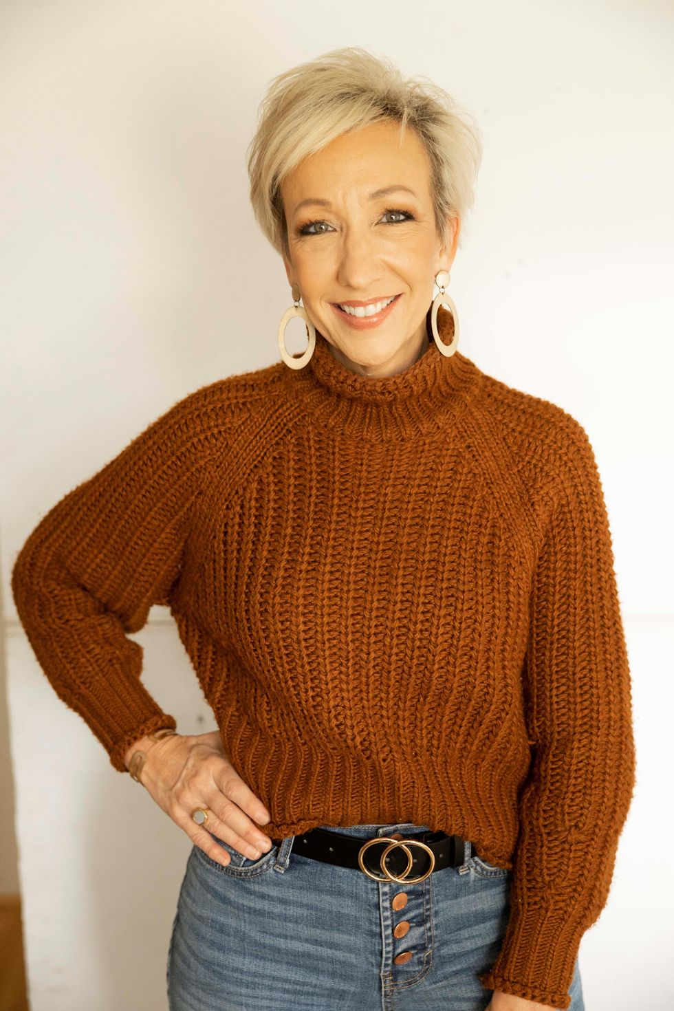 Photo of Dena Baughman, showing her in a rust-colored sweater and blue jeans, wearing gold hoop earrings.