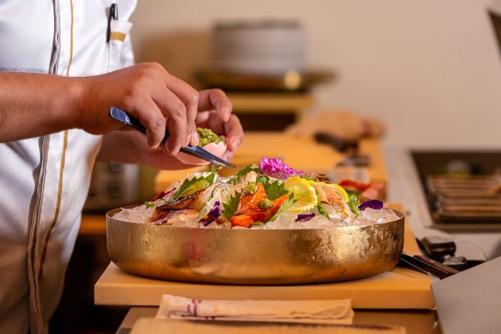 Photo of the hand of a chef, holding tweezers and garnishing a dish filled with ice and shellfish