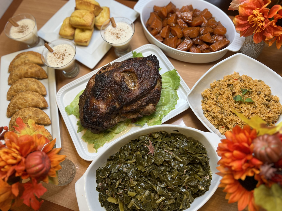 Picture of a bowl of collard greens, a fried Cajun turkey, a dish or rice and peas, and a dish of potatoes, set on a table with orange sunflowers.