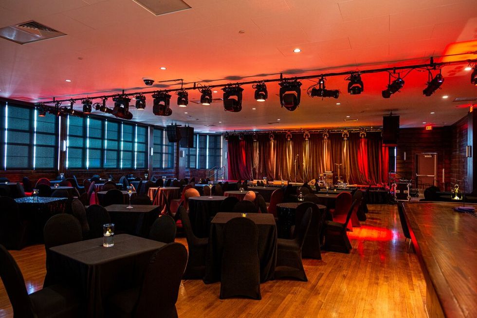 Picture of the interior of the Eldorado Ballroom, with black-clad tables ona hardwood floor, and a stage with red curtains at the back.
