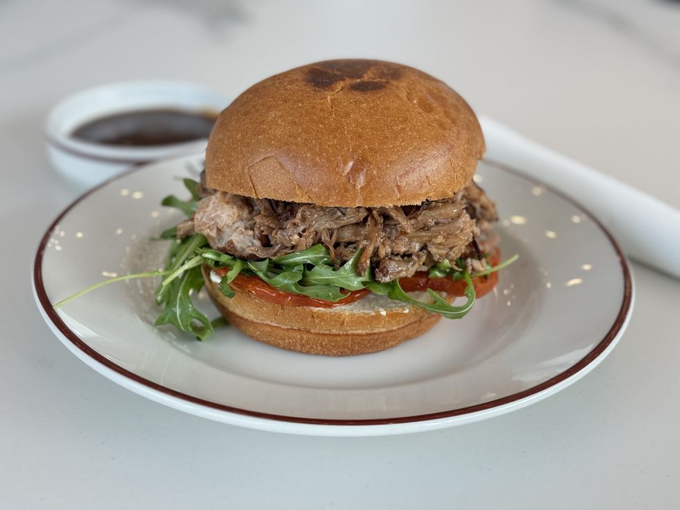 Pulled port sandwich on a wheat-looking bun with arugula sitting on a white plate.