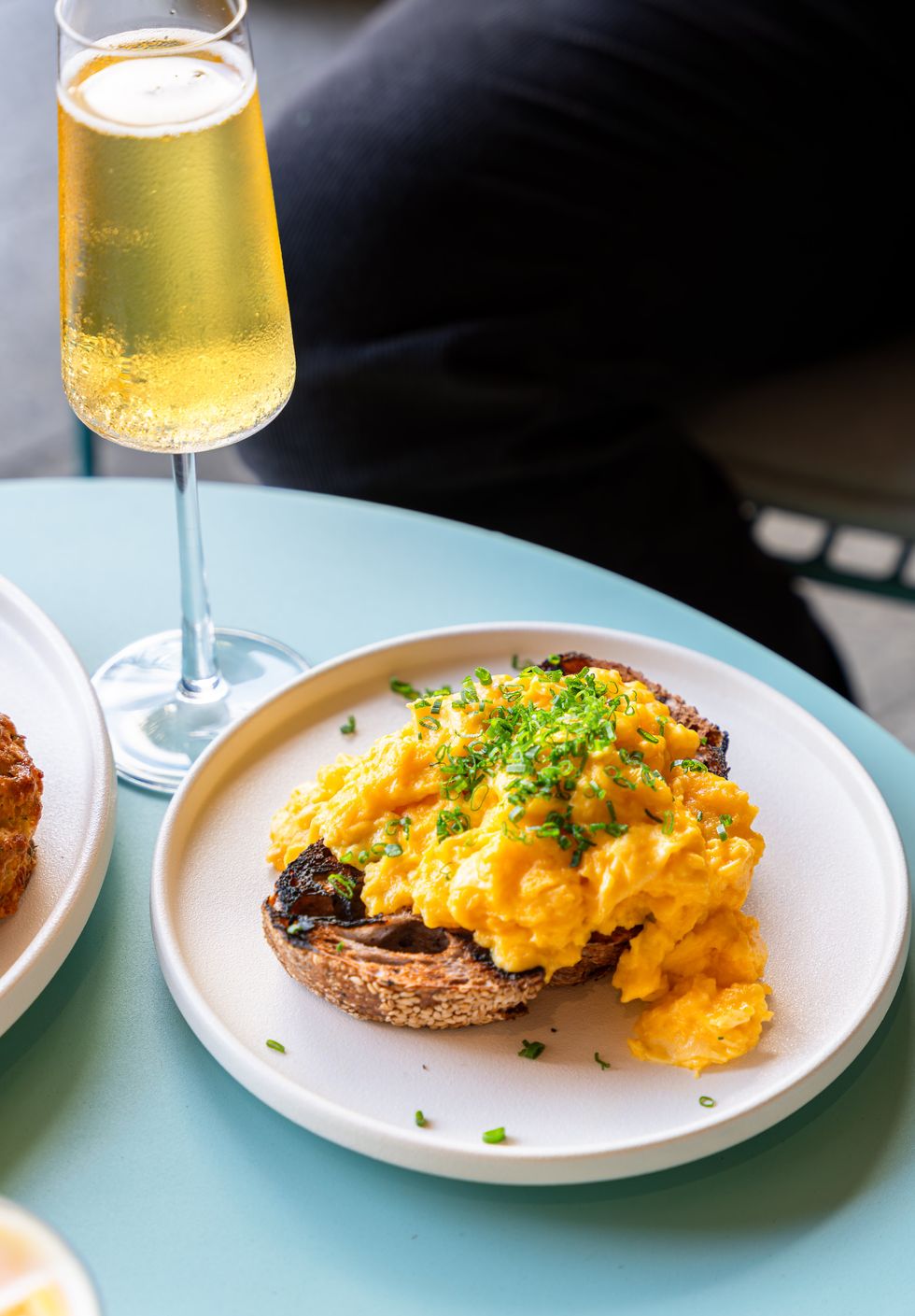 Scrambled egg on an English muffin sitting on a white plate. A glass of Champagne is next to the dish