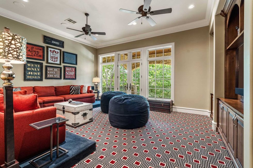 The game room of 50 Patti Lynn Lane shows built-in cabinetry, a red sectional couch and treetop views.