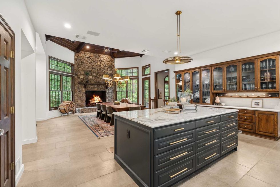 The kitchen of 23227 Brownwood Lane, showing a drawer-lined island overlooking the dining room with its dramatic stone fireplace