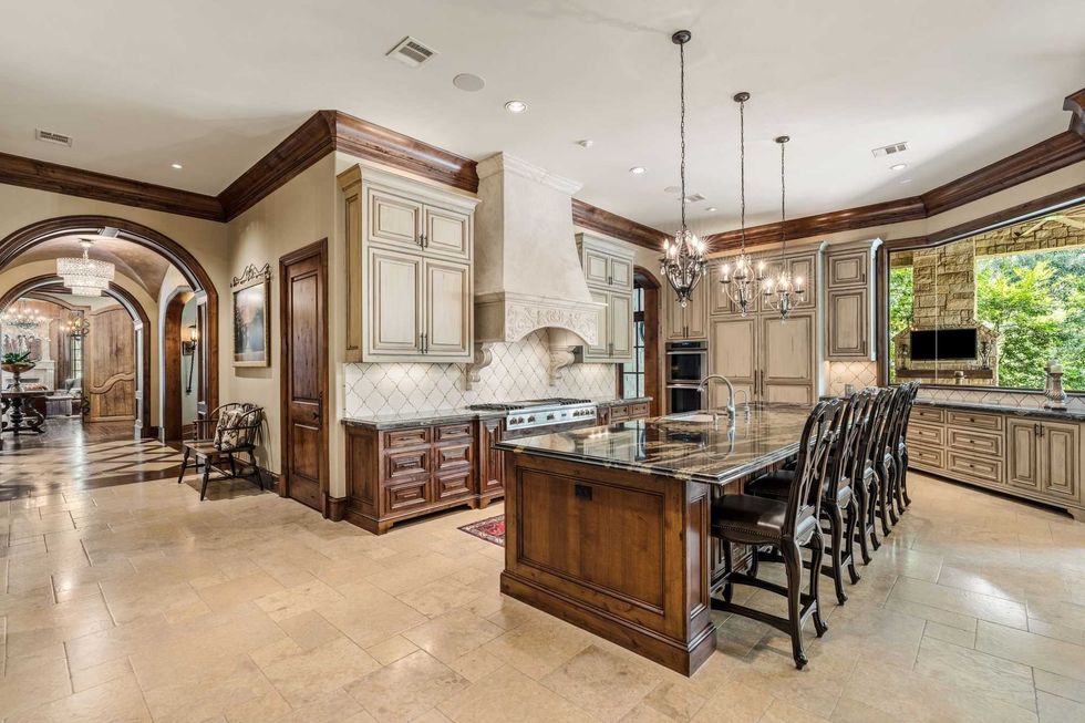 The kitchen of 50 Patti Lynn Lane with an island and chairs, a hooded range, and curving wall with woodland views