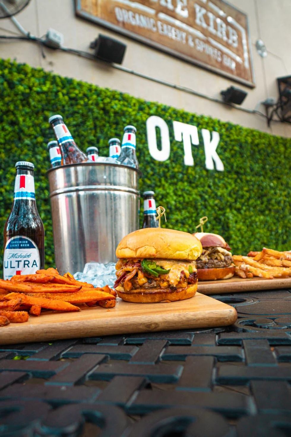 Two big burgers on wooden slabs with fries and buckets of beer.