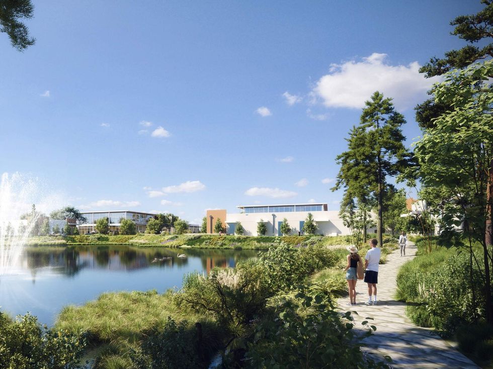 Two people walk a trail next to a lake with a housing development by Kirksey in the distance.