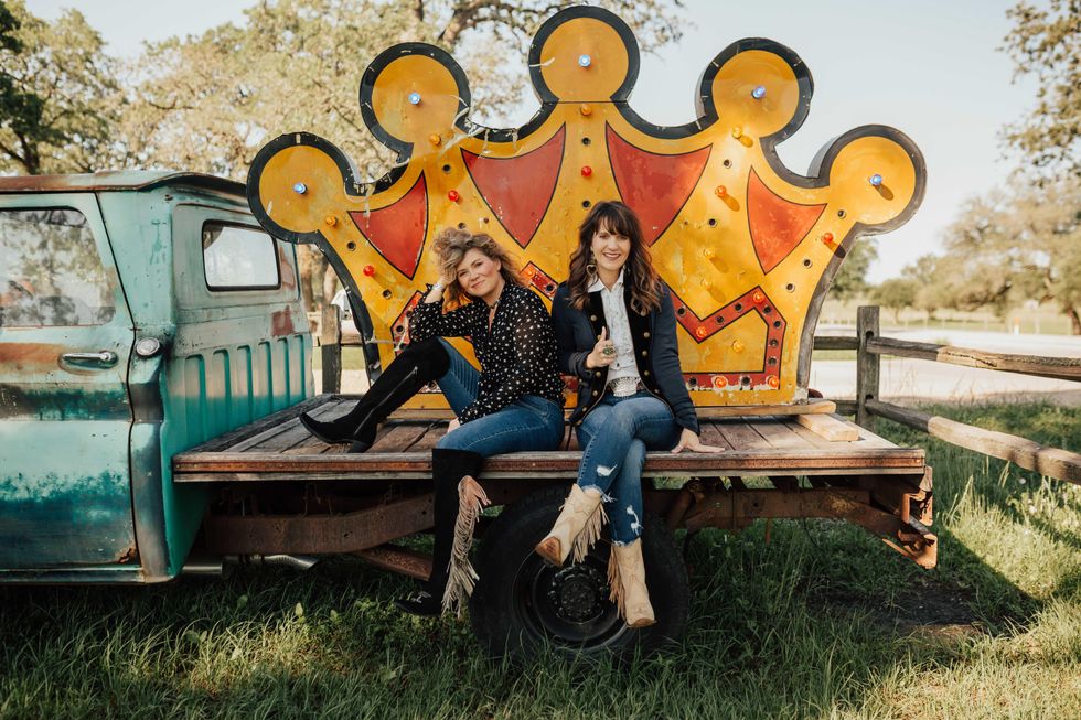 two women on a truck bed with a crown behind them