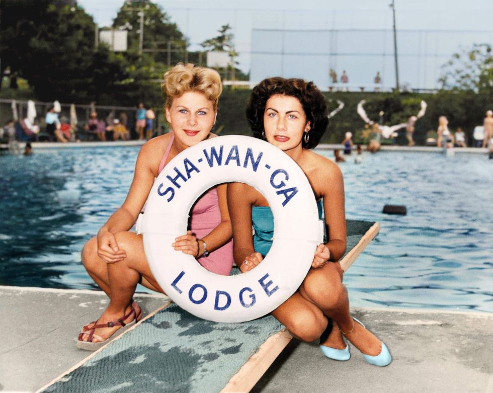 Two women sitting on a diving board holding a life preserver saying Sha-wan-ha Lodge