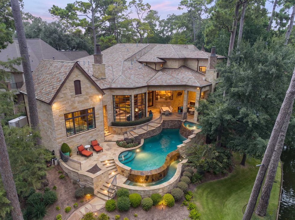 View of the backyard patio of 50 Patti Lynn Lane showing the multi-level pool and spa and a staircase leading down to wooded grounds
