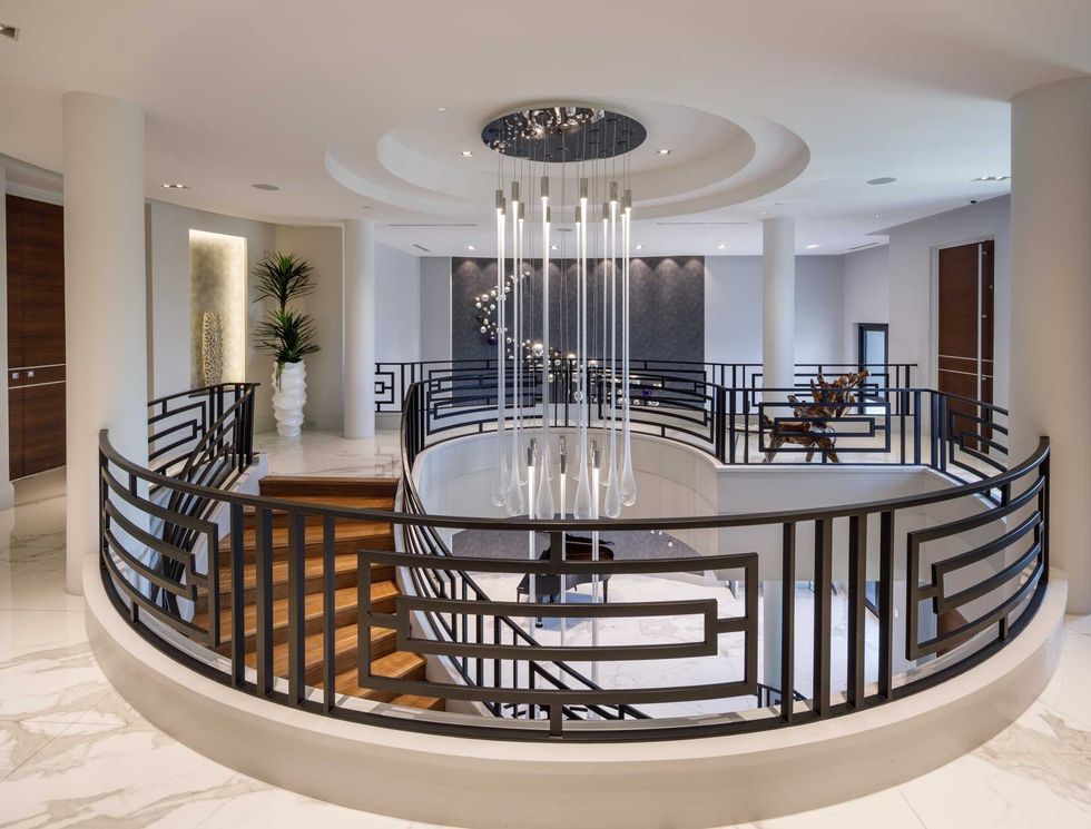 View of the living room in 3201 Noble Lakes Lane showing the curve of the staircase, a hanging chandelier and recessed ceiling