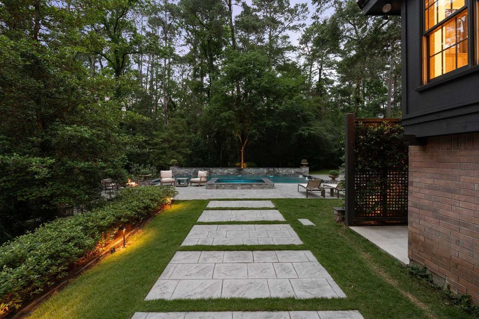 View of the pool and spa, with flagstone paving, grass, inset lighting and trees