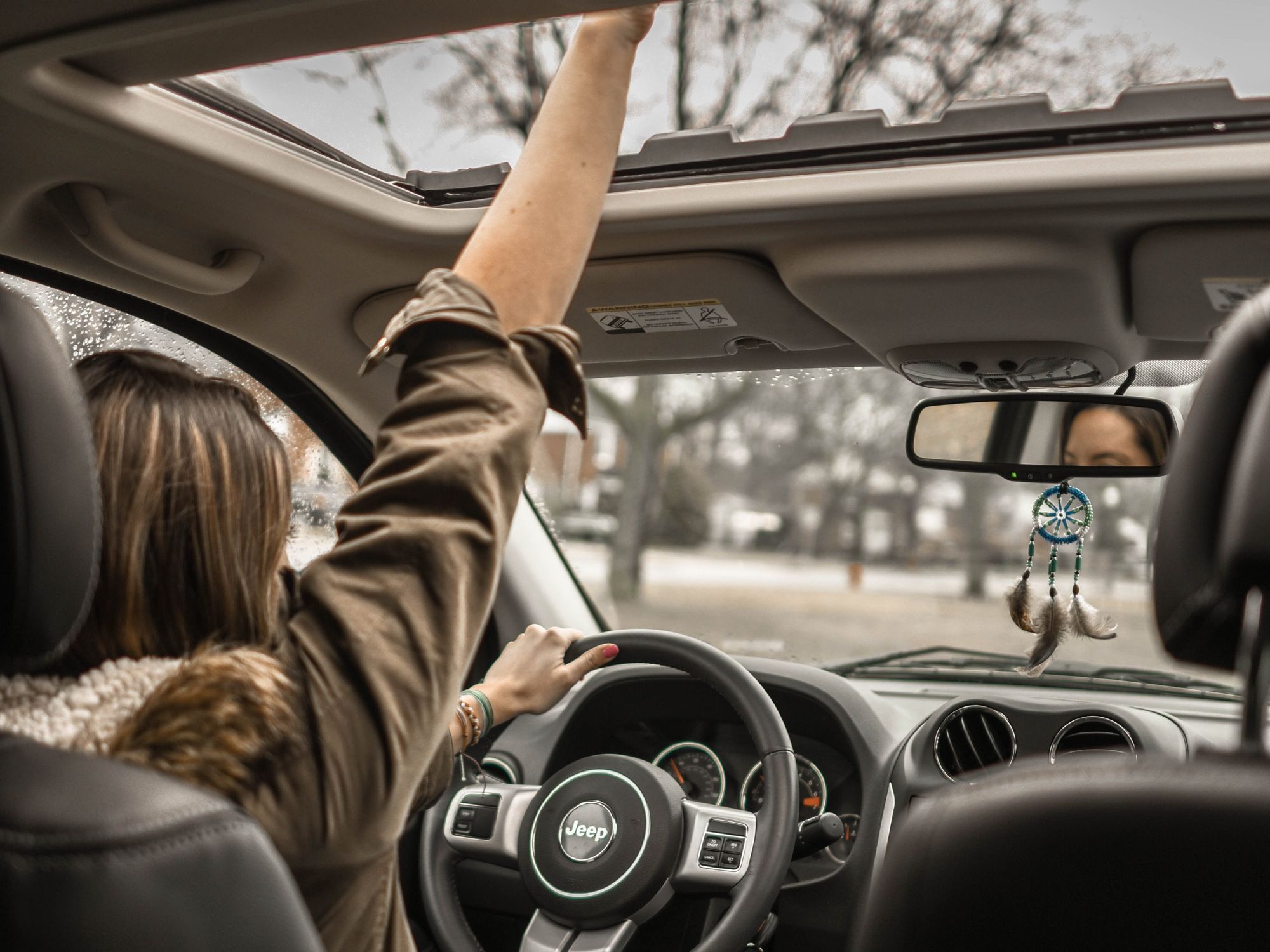 woman driving car raising fist sunroof 